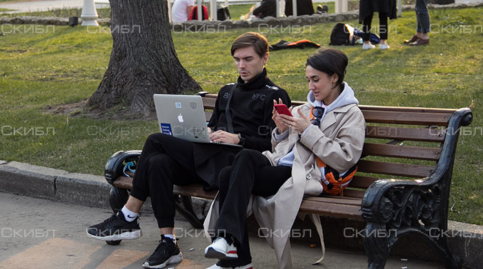 Девушка и парень сидят на скамейке, один с ноутбуков другой с мобильным